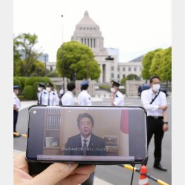 3日、スマートフォンの画面に映し出された、改憲派の会合に寄せられた安倍首相のビデオメッセージ。奥は国会議事堂（Ｃ）共同通信社