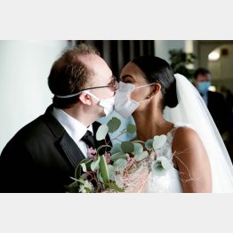 ゲストのいない結婚式で防護マスクを介してキスする新郎新婦（Ｃ）ロイター